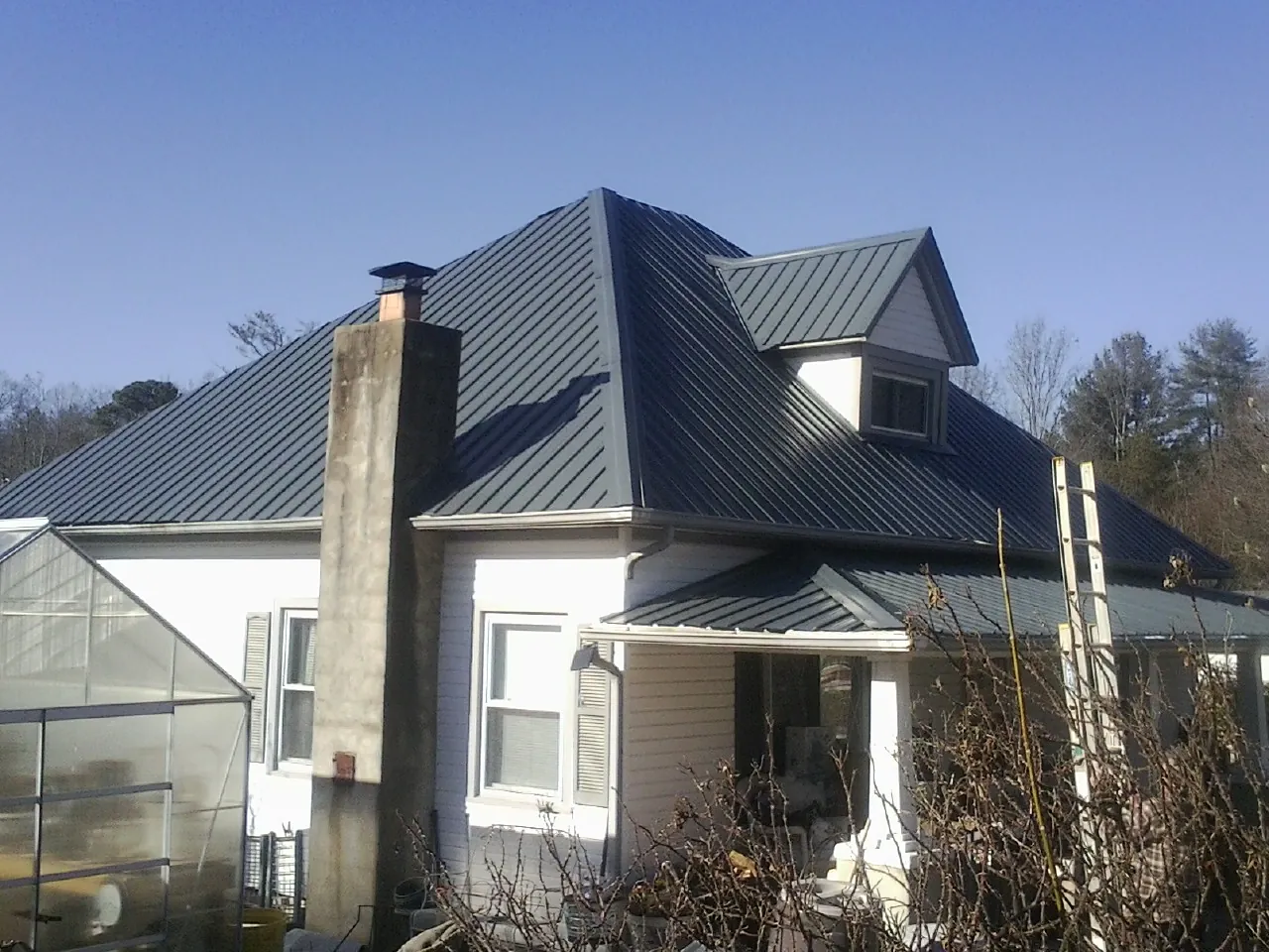 Dark blue standing seam metal roof on a white farmhouse with dormer — Slate & Tile Roof Repair by Roofing Brothers in Wake Forest