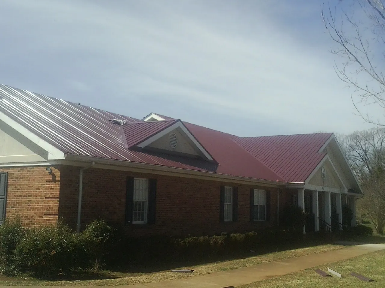 Red metal roof with gabled entries on a long brick building, from a Hail Damage Roof Repair job in Wake Forest