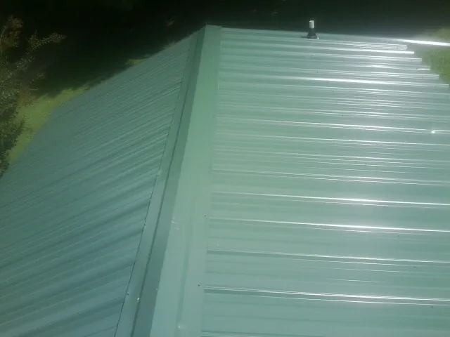 New green metal panels meeting at the ridge of a roof — Flat Roof Repair work by our crew in Wake Forest