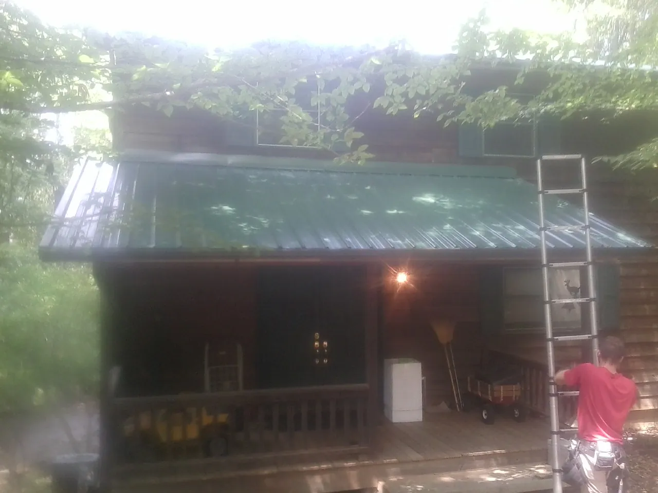 Worker on a ladder at the green porch roof of a wooded cabin in Wake Forest