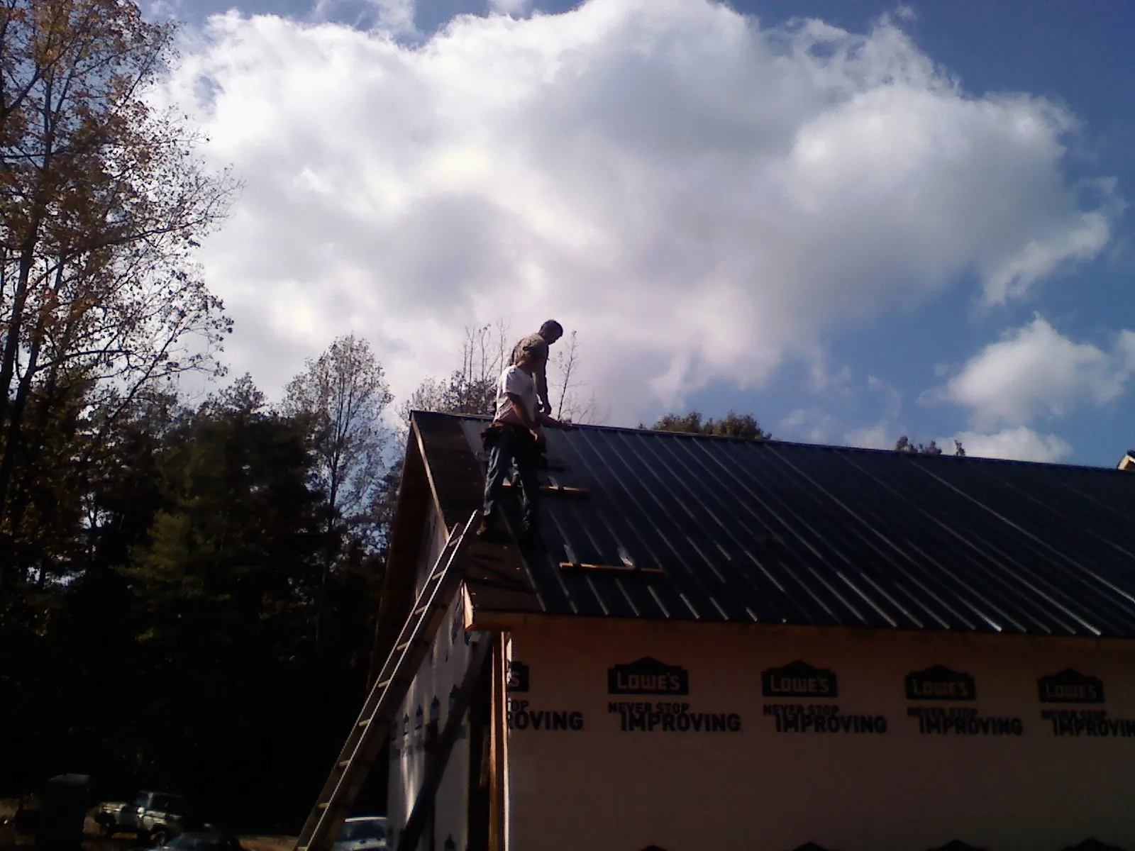 Roofer fastening dark metal panels high against a cloudy sky, from a Roof Inspection job in Wake Forest