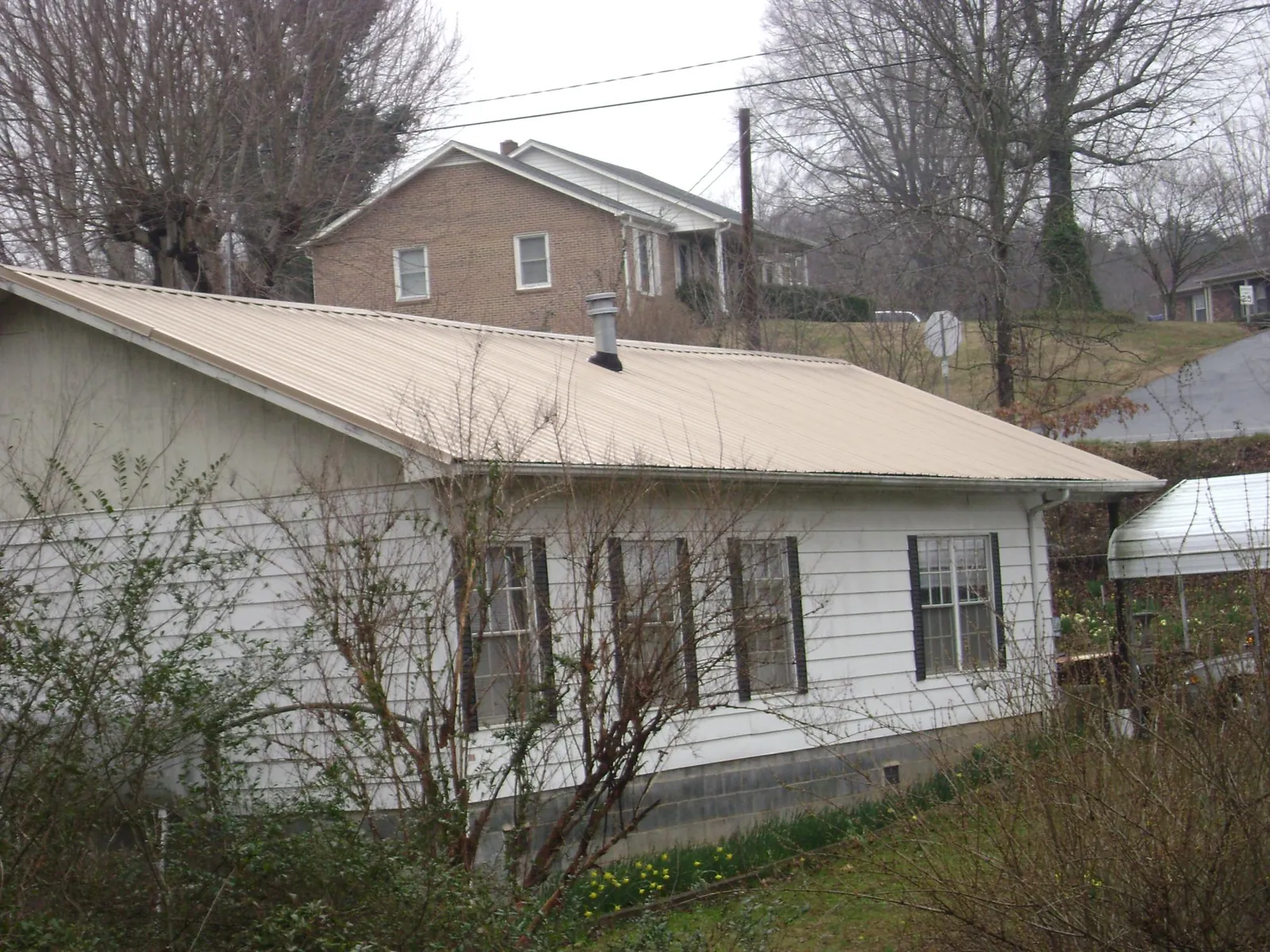 Tan metal roof on a white sided house set into a hillside — Commercial Roofing by Roofing Brothers in Wake Forest